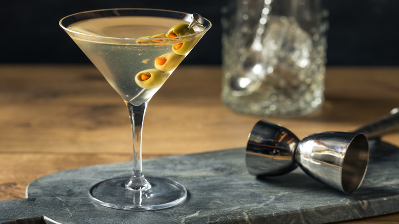 A dirty martini with stuffed olives on a cocktail stick served on a marble slate