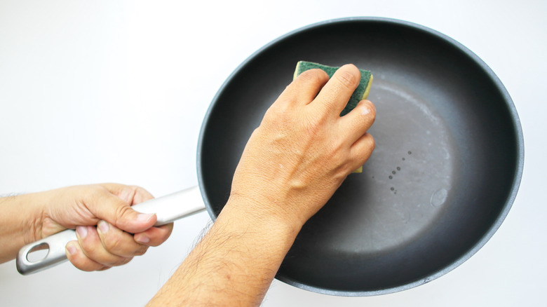 a man's hands hold up a nonstick pan while wiping it with a sponge