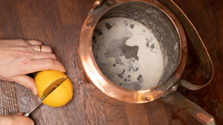 hands cutting a lemon in half next to copper pot