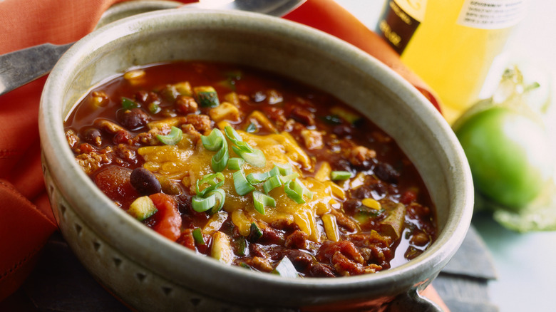 A bowl of chili with meat, cheese, beans, tomations, green onions, and other toppings