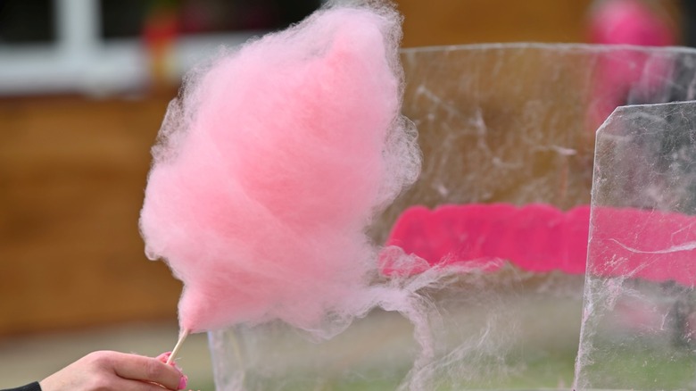 A hand lifting a stick of cotton candy out of the spinning machine