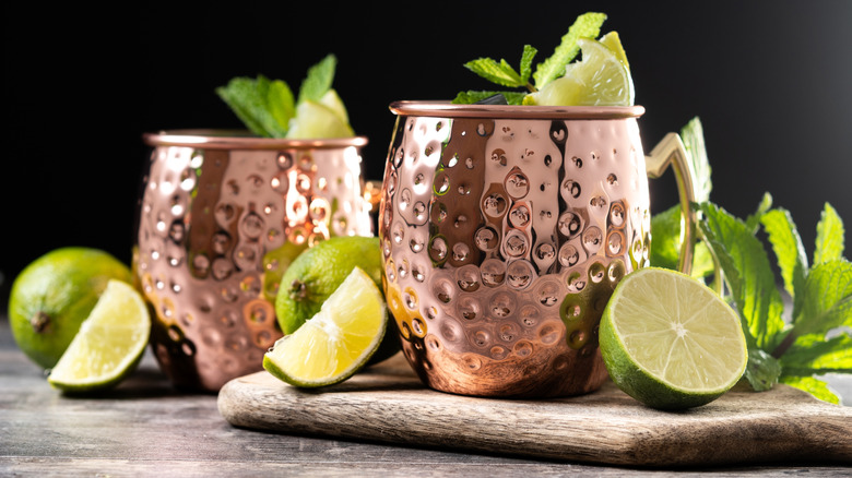 two copper mugs with limes and mint leaves