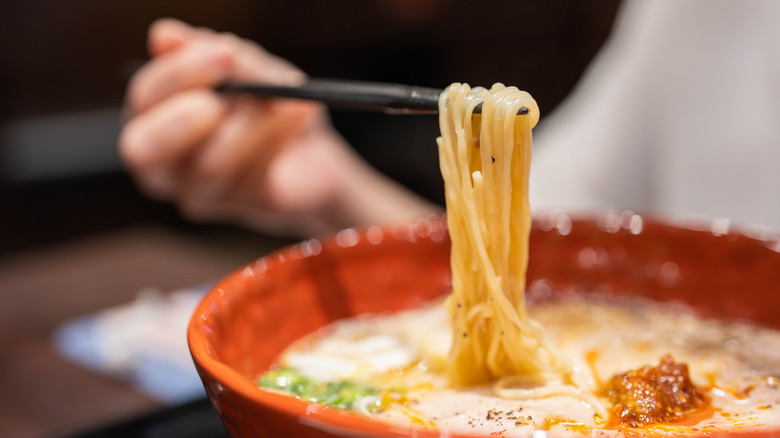 hand using chopsticks to lift ramen noodles out of a bowl