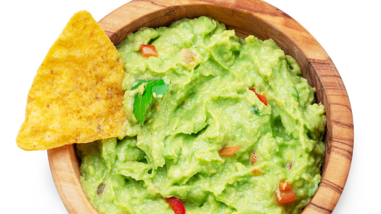 Guacamole in a wooden bowl with a triangular tortilla chip dipped in it.