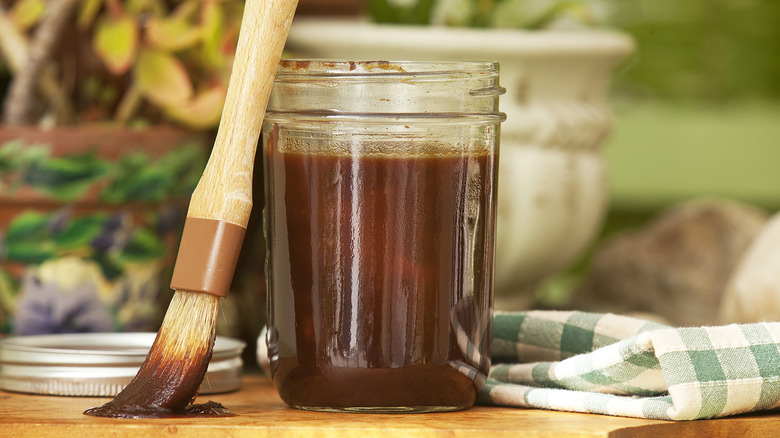 An open jar of homemade BBQ sauce with a used food brush leaning against it