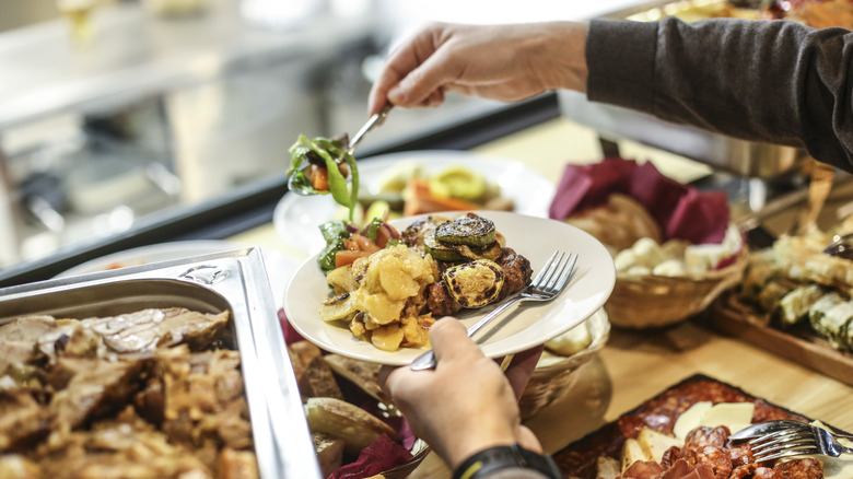 hands scooping vegetables onto plate from a buffet table