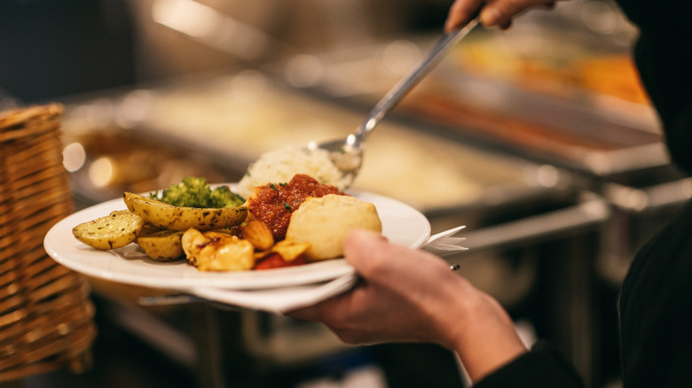 person spooning food onto a plate from a buffet