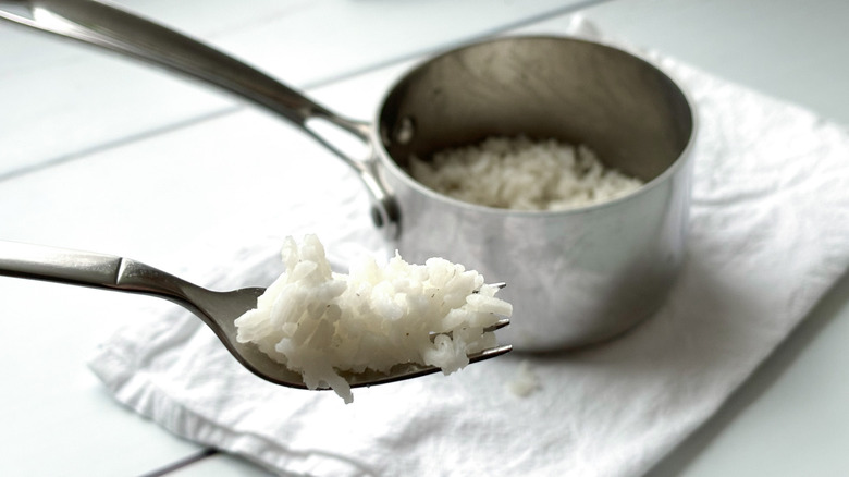 Silver saucepan with white rice on fork