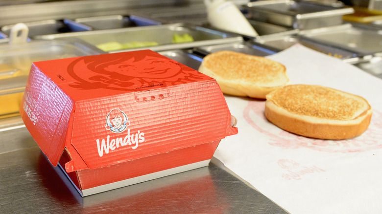 A red Wendy's box beside an open hamburger bun