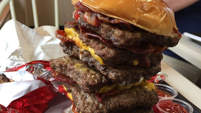 The T-Rex burger from Wendy's with its wrapper and ketchup beside it.