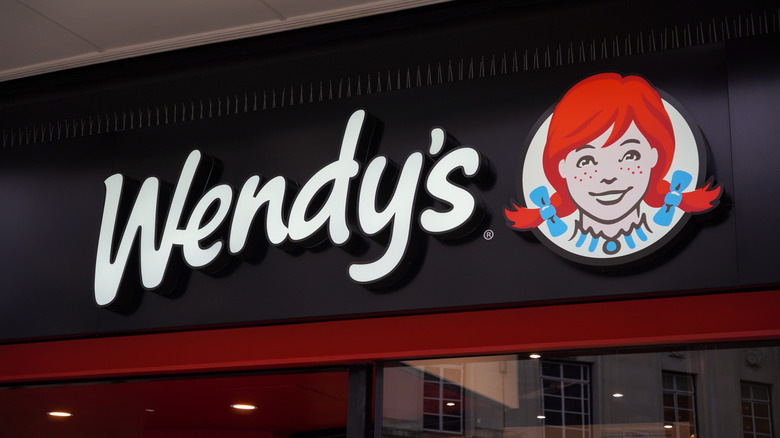 A Wendy's sign inside of a building on a black background above a window.