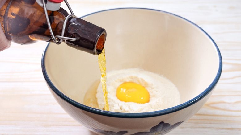 Someone pouring a bottle of beer into a bowl of egg batter