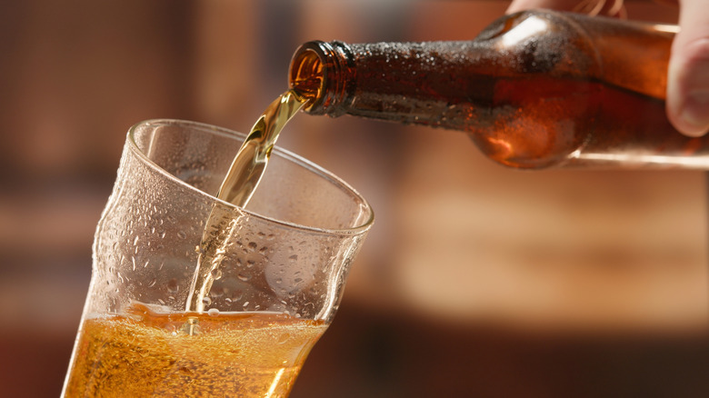 A close-up of a hand pouring a bottle of beer into a pint glass