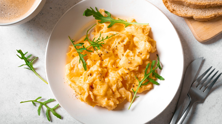 A plate of soft, fluffy, seasoned eggs garnished with fresh herbs and paired with toast