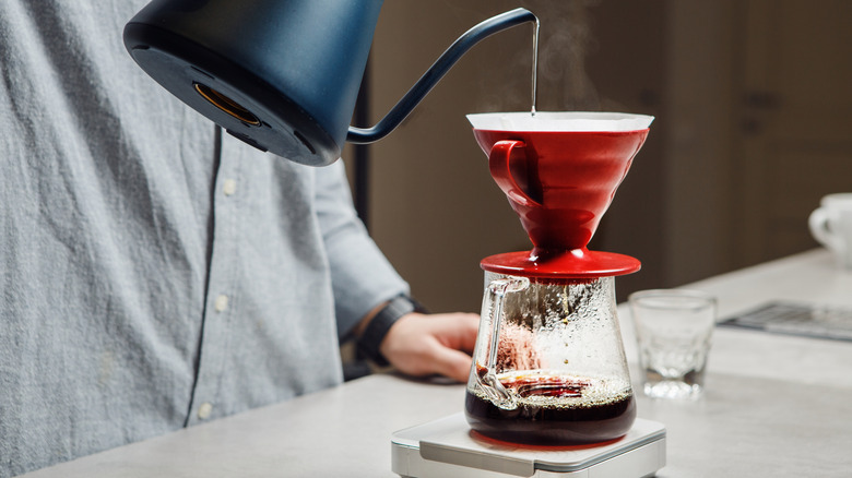 An individual pouring hot water from a kettle into a pour over carafe on a coffee scale