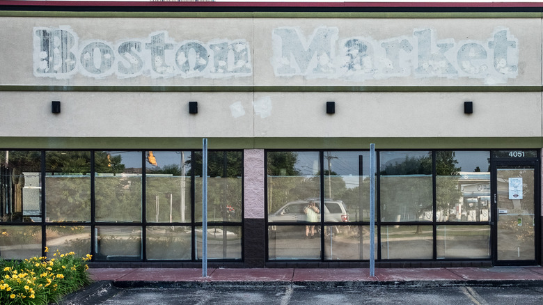 Storefront of a closed Boston Market restaurant. Windows papered over and signage gone