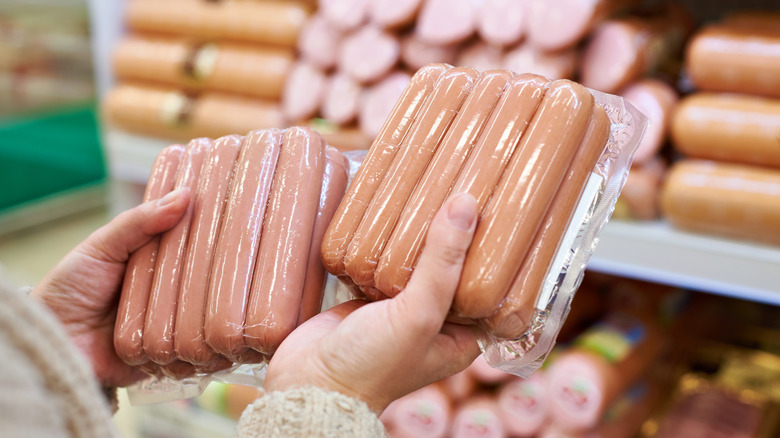 woman at grocery store holding and deciding between two packages of hot dogs