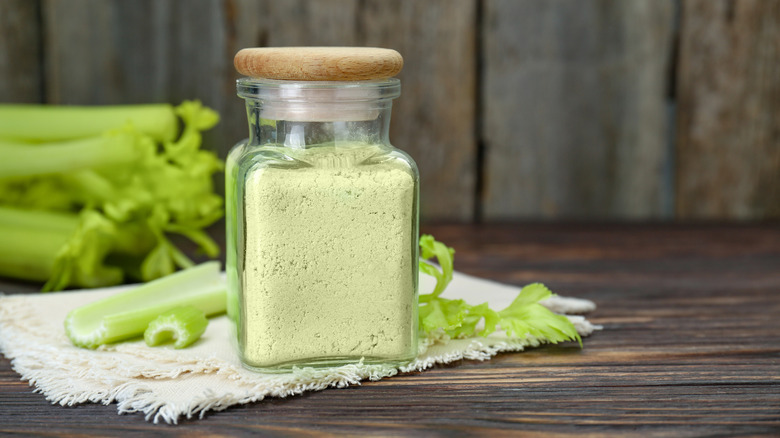 Natural celery powder in a jar and fresh stalks in the background