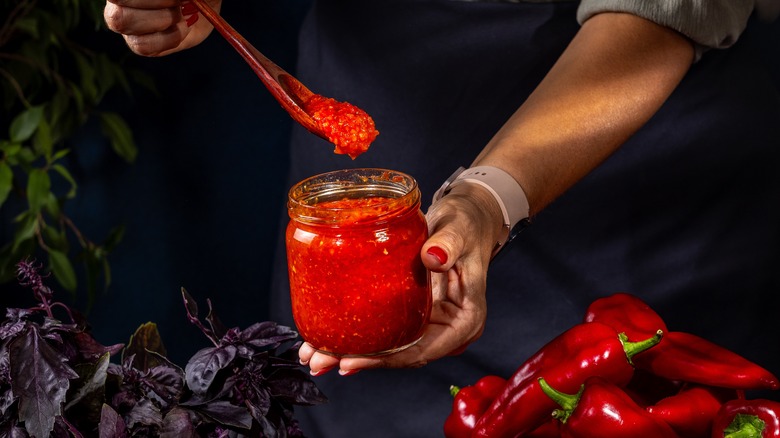 Person taking of spoonful of ajvar from a glass jar