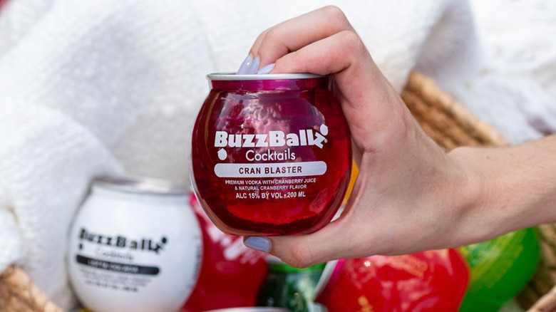 woman holds a can of BuzzBallz Cocktail Cran Blaster above basket of various flavored BuzzBallz