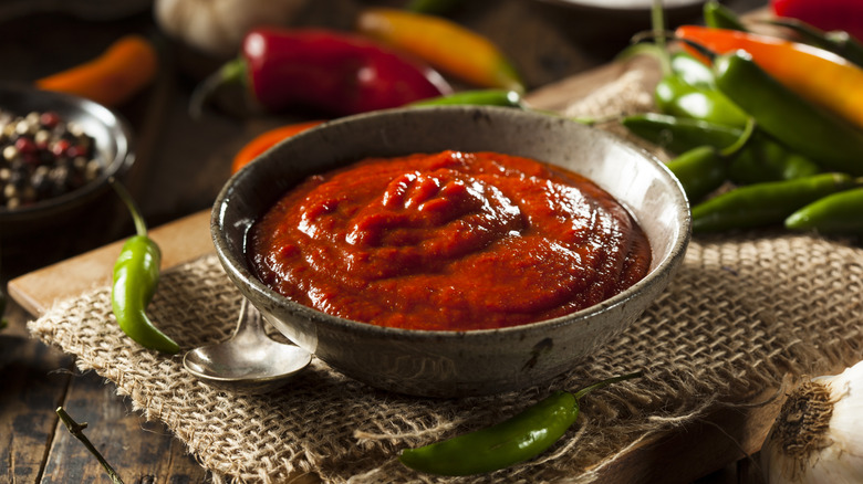 Sriracha sauce in a bowl with peppers around