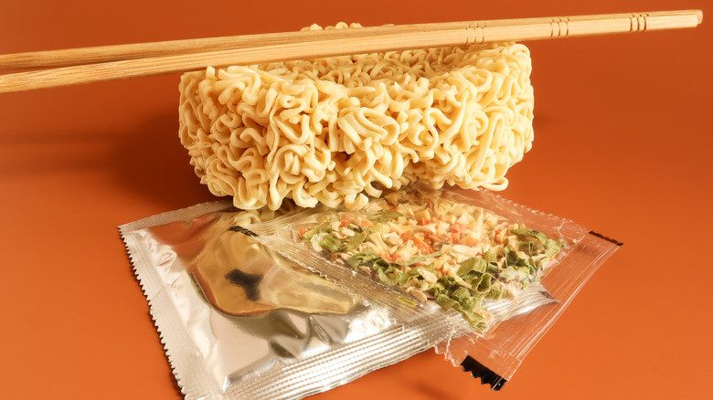 Uncooked instant ramen noodles with seasoning packets and chopsticks.