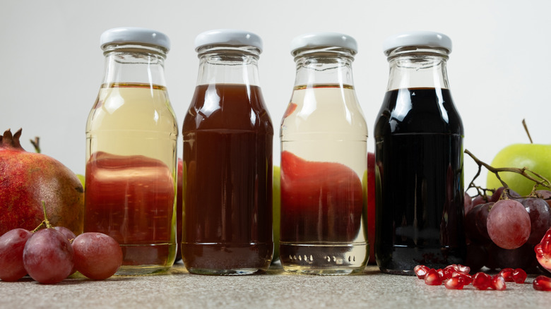 Different vinegars in glass bottles surrounded by fresh fruit