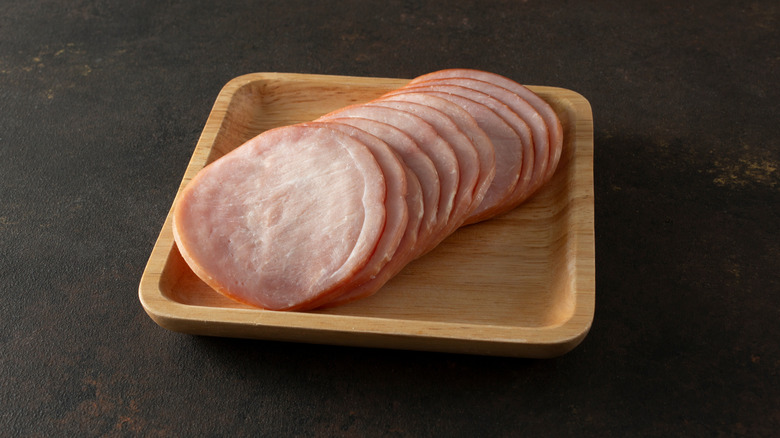 Sliced Canadian bacon on a wooden plate.