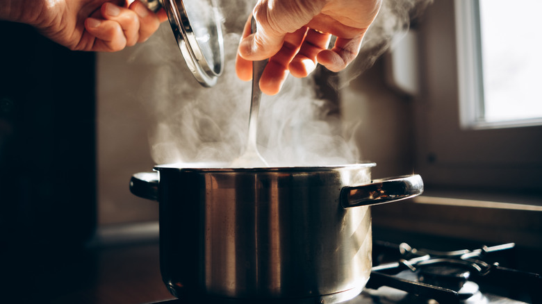 hand with spoon stirring steaming pot on stovetop