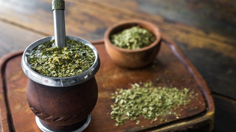 A cup of yerba mate with straw and dry mate in background.