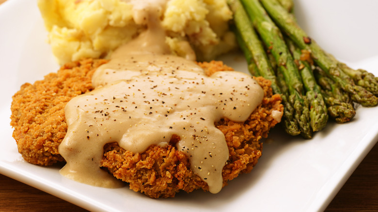 Country-fried steak with brownish gravy, potatoes, and asparagus.