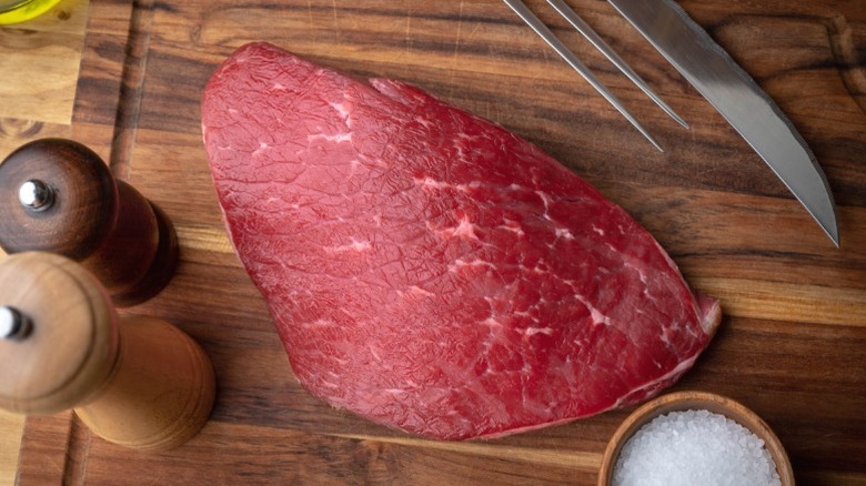 A raw piece of flank steak on a wooden cutting board with seasoning