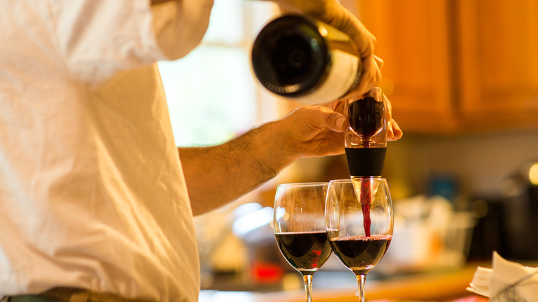 Man in a kitchen pours red wine into a glass using an aerator