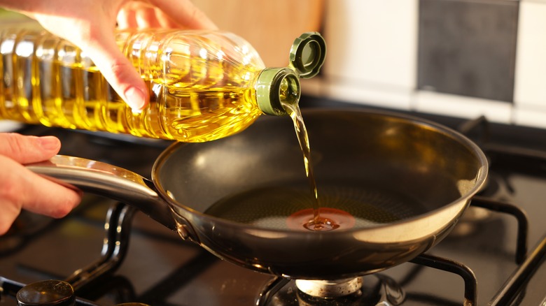 hands pouring oil into a skillet on the stove