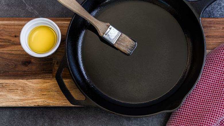 a cast iron skillet on a wooden table being brushed with some oil