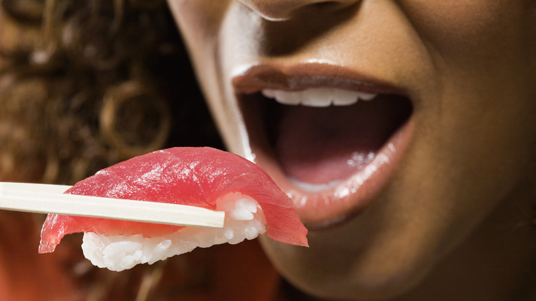 Someone about to bite into a piece of raw sushi