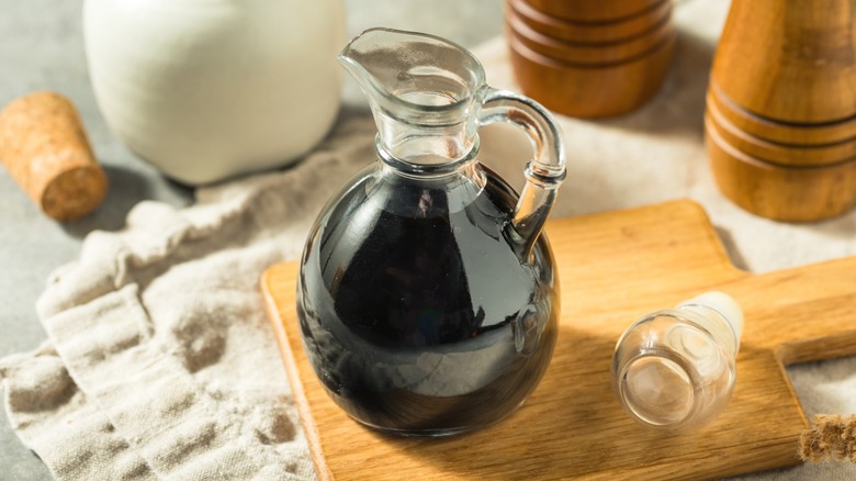 A glass jug of balsamic vinegar on a wooden cutting board