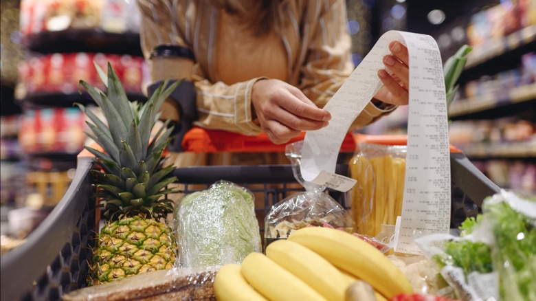 Shopper checking grocery reciept with cart of groceries