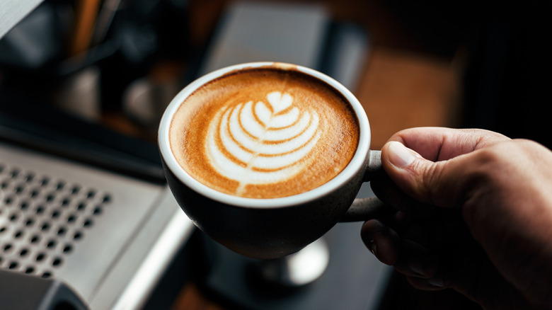 a hand holding an espresso with latte art