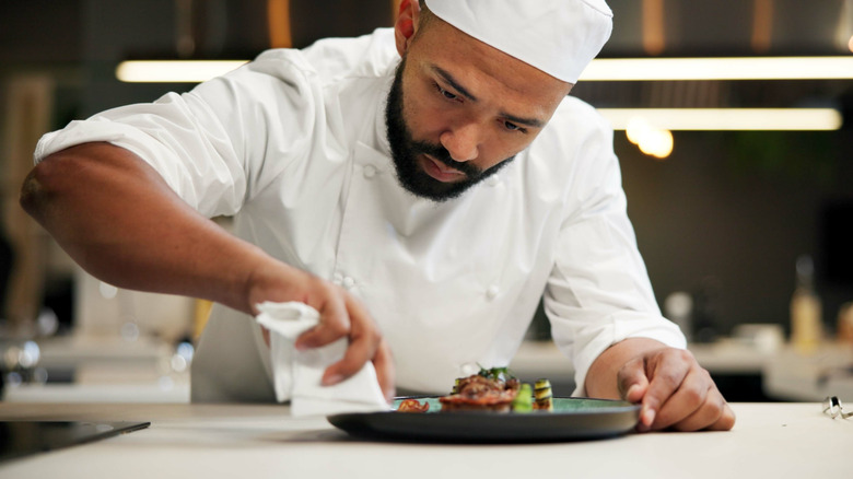 A male chef wiping the edge of a plate of food