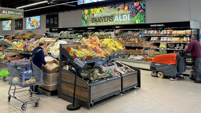 produce section of an Aldi grocery store with a woman shopping and a man cleaning the floors