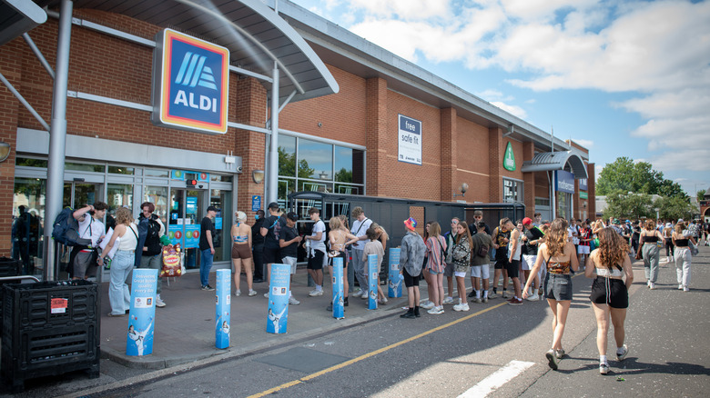 A large line of people awaiting entry into an Aldi location during the day