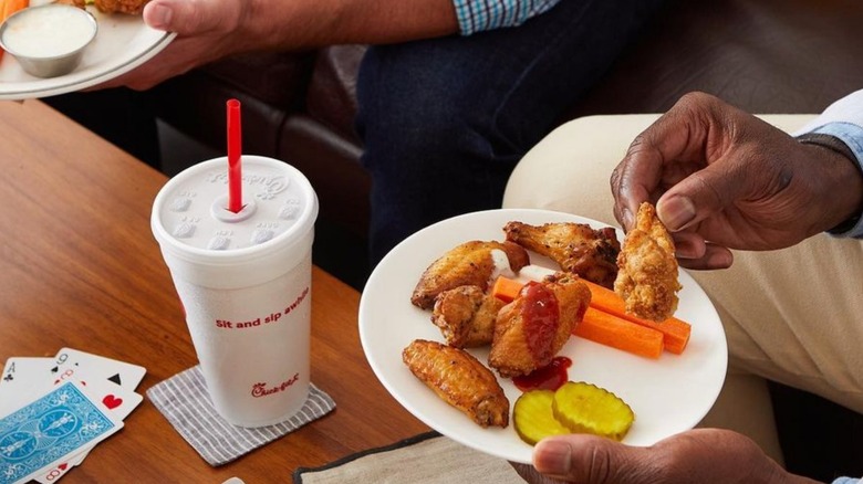 person eating Little Blue Menu wings with Chick-fil-A drink