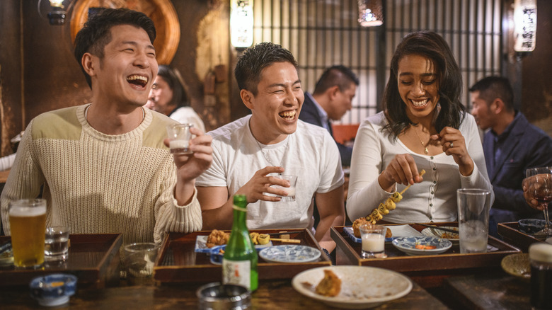 Three people eating, laughing, drinking at izakaya