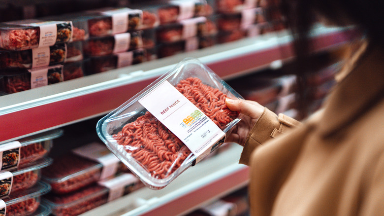 someone holding a ground beef package at a grocery store