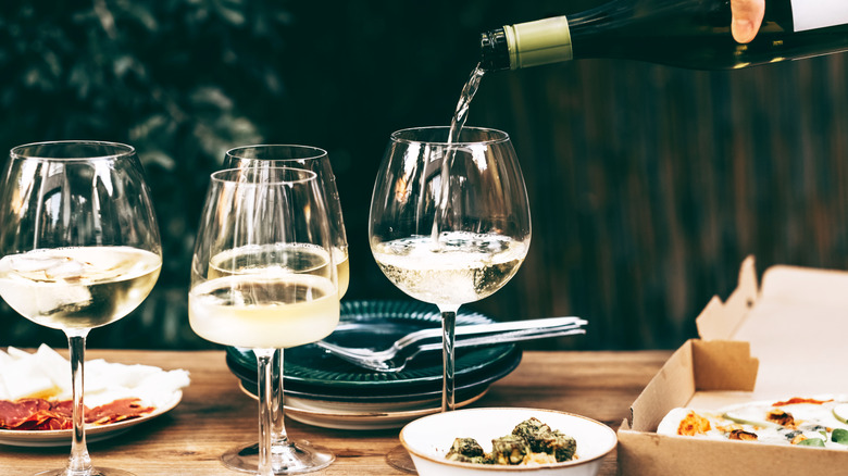 Pouring white wine into stem glasses on a table