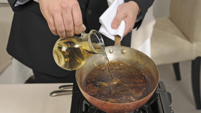 person pours liquid into a pan to deglaze