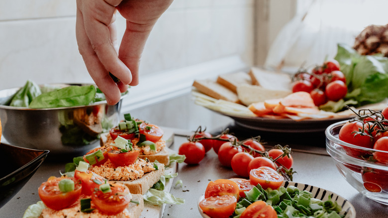 Sprinkling herbs on fresh tomatoes and toast