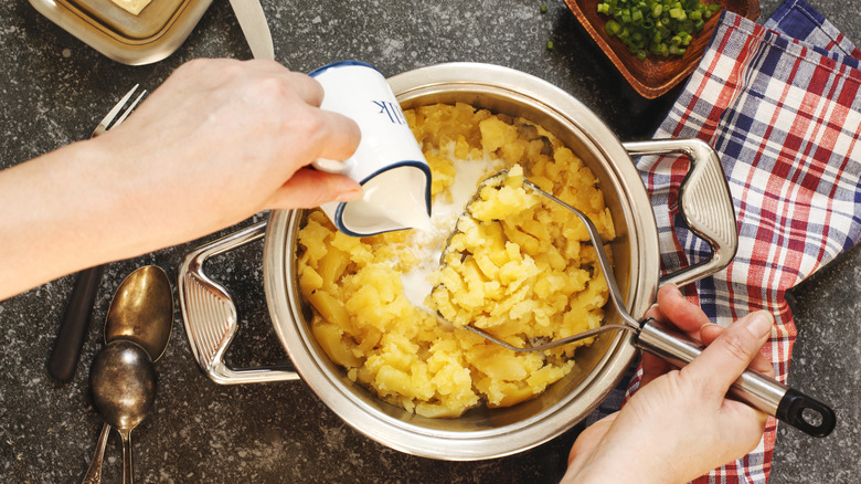 Top down view of hand pouring milk into bowl of mashed potatoes