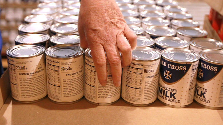 Hand taking a can of evaporated milk from a row of cans